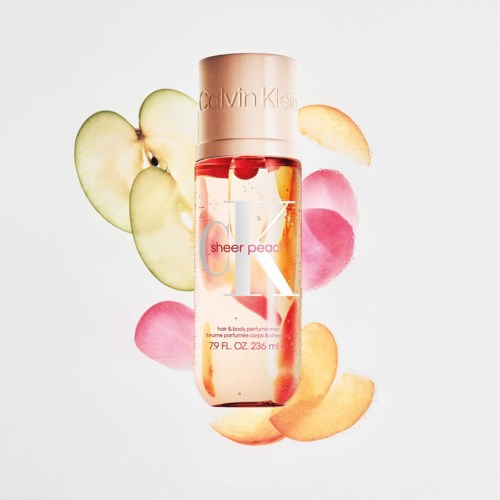 Calvin Klein Sheer Peach kroppsfukten med skiver av fersken og rosa, oransje og grønne blad rundt den.