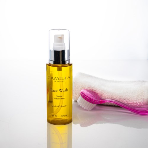 Eine gelbe Flasche Gesichtsreinigung mit einem weißen Handtuch und einer pinken Zahnbürste daneben.