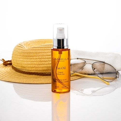 Eine Flasche Bräunungsöl, ein Sonnenhut, Sonnenbrille und ein weißes Handtuch sind zusammen arrangiert.