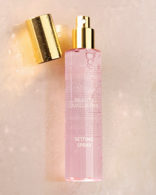 Een roze glazen fles met gouden spraydop en bijpassende gouden dop, gemarkeerd 'Camilla Phil Setting Spray.'