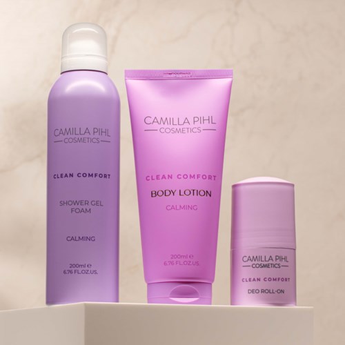 Tre lilla lilafargede Camilla Pihl Cosmetics Clean Comfort produkter: dusjsåpe, kroppslotion og deodorant roll-on.
