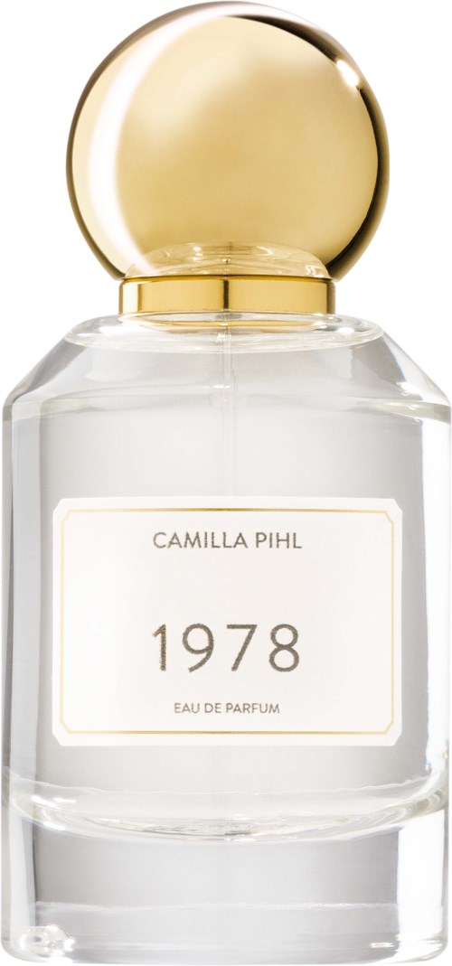 Przezroczysta butelka perfum z okrągłą złotą zakrętką, oznaczona "1978" od Camilla Pihl, wygląda elegancko i lśniąco.