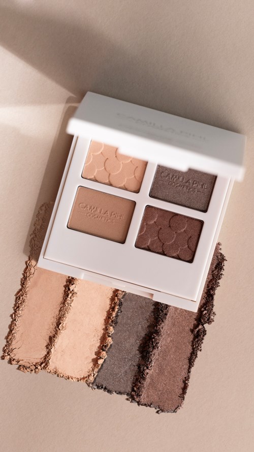 Een kleine_make-uppalette met vier oogschaduwen in beige, bruin en roze tinten. Stalen van deze kleuren zijn op papier.