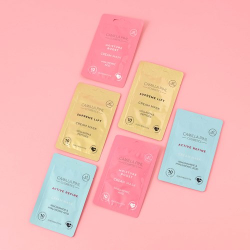 Sex färgglada ansikts maskpåsar placerade på en rosa bakgrund, med två rosa, två gula och två blå påsar.