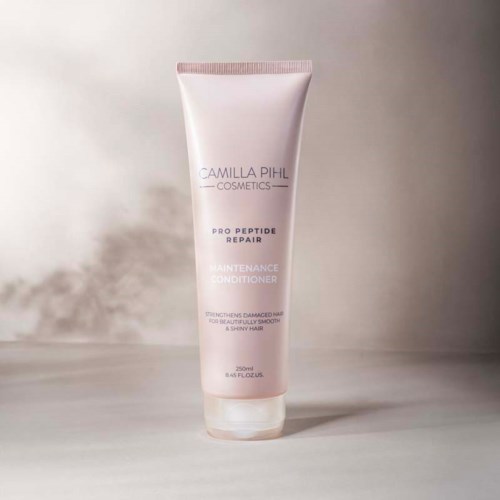A white tube of Camilla Pihl Cosmetics Pro Peptide Repair Maintenance Conditioner stands upright on a surface.