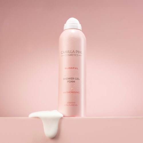 Pink shower gel foam bottle with lotion spill beside it on a pink background.