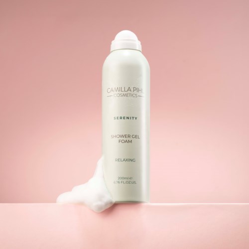 Witte fles van Camilla Pih Cosmetics Serenity douchegelfoam met schuim die eruit stroomt.