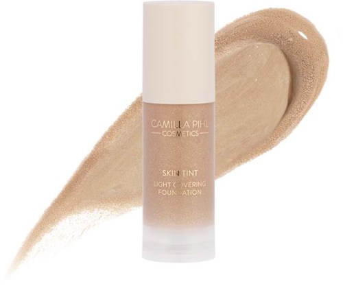 Eine Foundationflasche mit der Aufschrift 'Camilla Pihl Cosmetics Skin Tint' vor einem beigefarbenen Hintergrund.