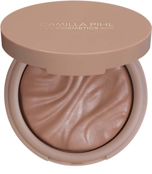 Een ronde compact met een lichtbeige deksel met de tekst 'Camilla Pihl Cosmetics', met glanzende, golfvormige make-up.