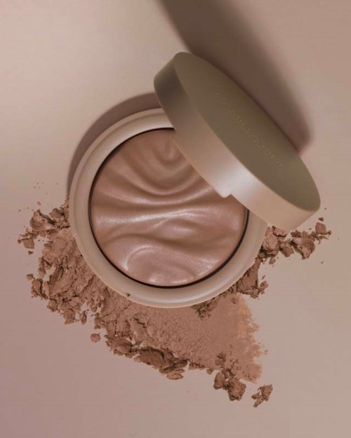 Een crème of make-up in een ronde container met een beige tint, omgeven door gebroken poeder.