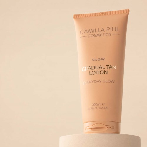 En ferskenfarget tube med Camilla Pihl Cosmetics glow lotion som står på en hvit overflate.