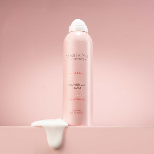 Pink shower gel foam bottle labeled Camilla Pihl Cosmetics Blissful. Foam spilled on surface below.