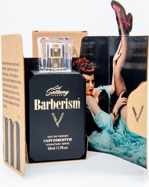 A perfume bottle labeled 'Barberism' with boxes and artwork behind it.