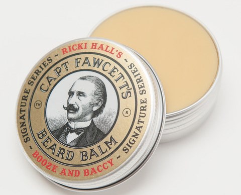 A round tin of beard balm with a vintage-style label featuring a man with a mustache, brand name, and flavor.