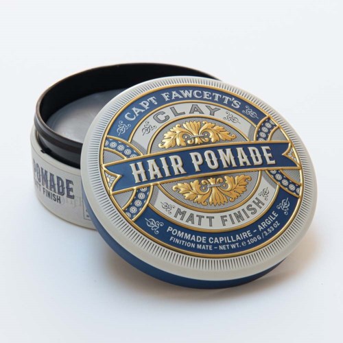 Round container of hair pomade with decorative blue and gold design, open to show the product inside.