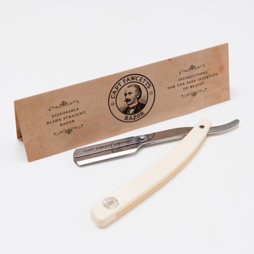 A straight razor with cream handle, in front of a vintage-style paper guide with logo and instructions.