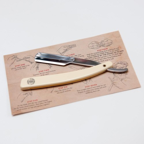 Two straight razors with handles, placed on a paper with shaving instructions and illustrations.