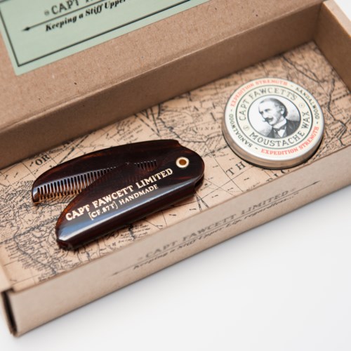 A vintage-style beard comb and a circular badge with a man's face and text inside a cardboard box.