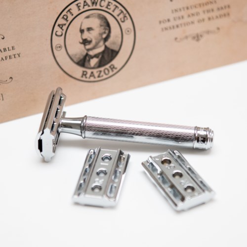 A vintage safety razor with two extra blades displayed on a white surface, near a paper with a logo of a man.