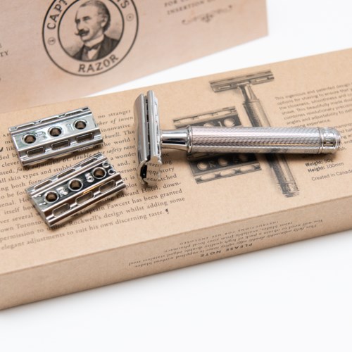 A safety razor with metal parts placed on a paper box with text and an illustration.