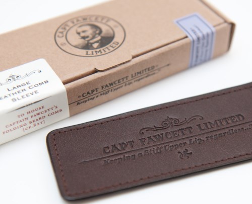 A leather wallet and a cardboard box with a man’s face logo and text, indicating a brand for accessories.