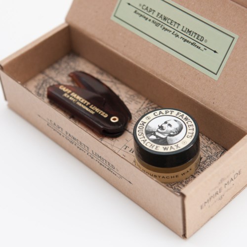 A box contains a moustache wax jar, a small tool, and a label with brand information.