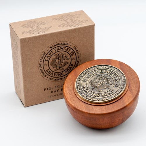 A round soap with a wooden case and a metal lid, and a tan box with text describing the soap.