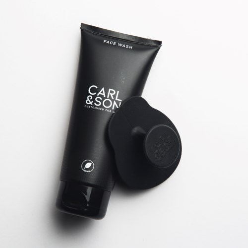A black tube of face wash labeled Carl & Son and a black facial cleansing brush.