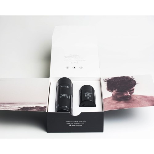 A black bottle, a black container, and a photo of a man with curly hair in a white box.