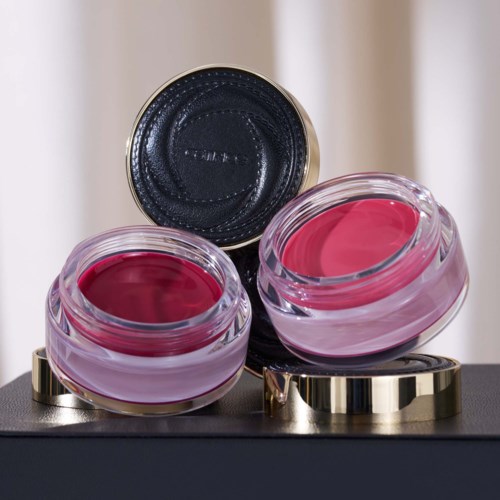 Two open pinkish lip balms or creams in glass jars with silver bases, placed on a black surface.