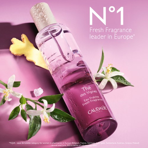 Pinkki hajuvesipullo kukkineen ja inkiväärin kanssa vaaleanpunaisella taustalla, mainostaen Caudalieä, ranskalaista tuoksumerkkiä.