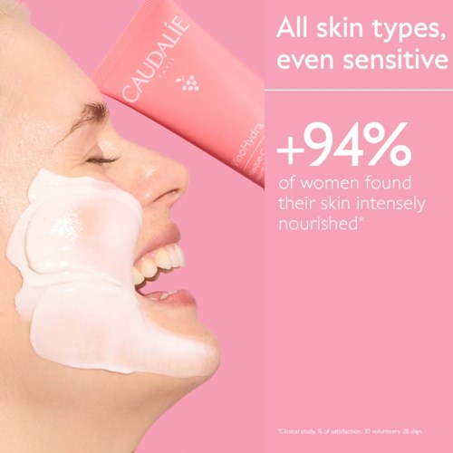 A woman with a big smile has white cream on her cheek, advertising a skincare product for all skin types.