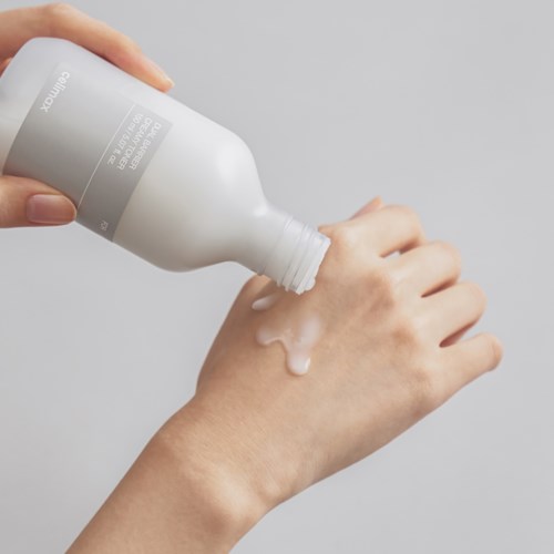 A person pours liquid soap onto their hand from a white bottle.