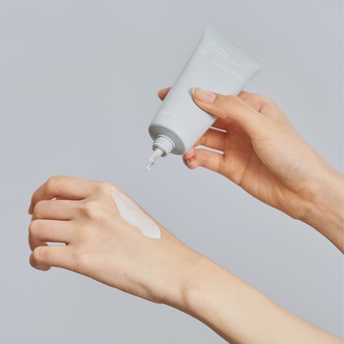 Eine Person trägt Creme oder Lotion auf die Hand aus einer Tube in einer schlichten Umgebung auf.