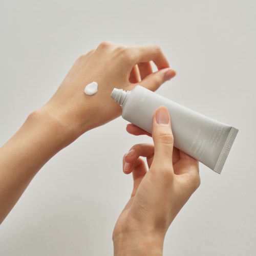 Eine Person drückt weiße Creme aus einer Tube auf die Hand.