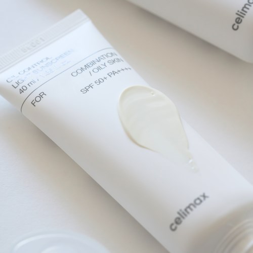 A white tube with cream and black text, placed on a white surface, likely a skincare product.