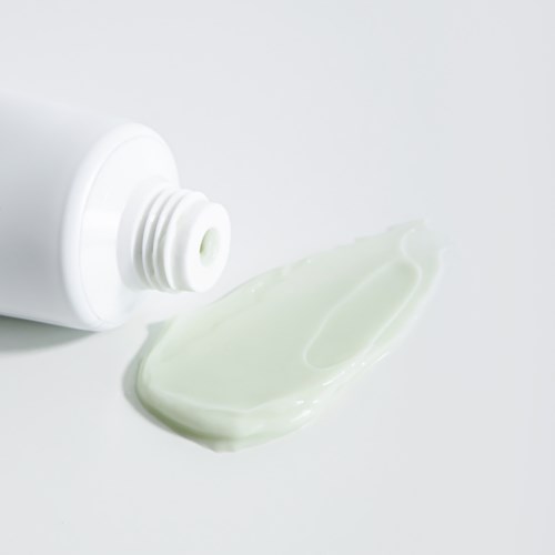 Eine weiße Tube mit Creme, die auf eine weiße Oberfläche herauskommt. Die Tube ist geöffnet und die Creme ist verteilt.