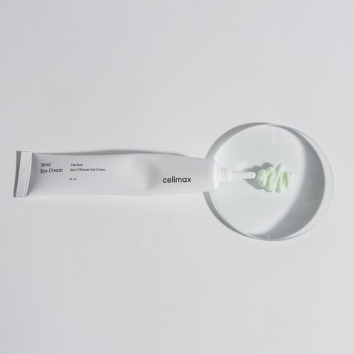 Eine Tube Augencreme neben einem Teller mit etwas Creme auf weißer Oberfläche.