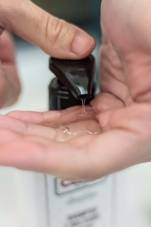 Someone dispenses liquid soap into their hand from a bottle. The focus is on handwashing and cleanliness.