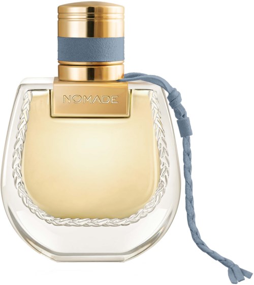 Een parfumfles met een gouden dop, doorzichtig glas en een blauw lint aan de zijkant. Het label zegt "NOMADE."