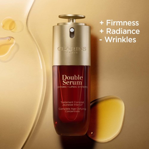A red serum bottle from Clarins with a gold pump, surrounded by drops of serum and a yellow background.