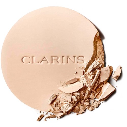 A round compact powder with the brand name 'Clarins' embossed, partially broken with scattered powder pieces.