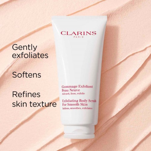 Een witte tube met Clarins exfoliërende lichaamscrème met roze tekst, op een geribbelde perzikkleurige achtergrond.