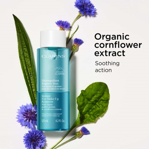 Das Bild zeigt eine blaue Flasche mit Augen-Make-up-Entferner, umgeben von lila Blumen und grünen Blättern.