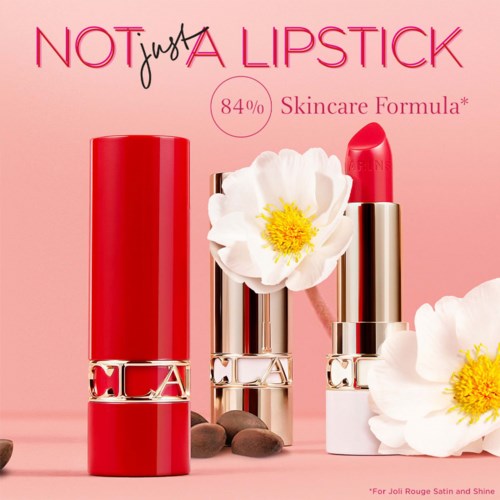 A lipstick and a lipstick cap with flowers, stones, and text about skincare and lipstick, on a pink background.