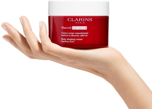 Een hand houdt een rood potje met Clarins lichaamsvormende crème met een witte deksel.