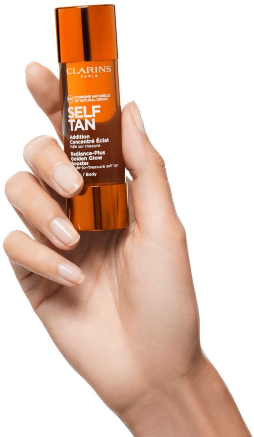Eine Hand hält eine kleine orangefarbene Flasche mit dem Label Clarins Self Tanning, mit goldener Kappe, in einem klaren Produktfoto.