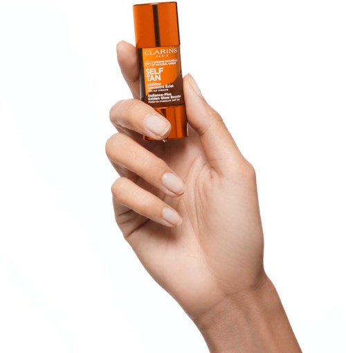 Eine Hand hält eine kleine orange Flasche des Clarins Selbstbräunungsprodukts.