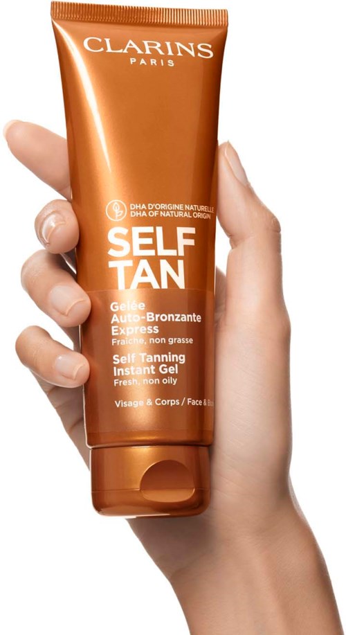 A hand holds a brown tube labeled 'Clarins Self Tan Gel' for a sunless tan.