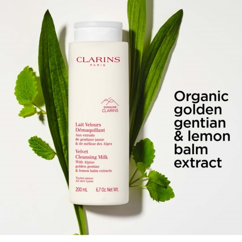 A white bottle labeled Clarins, surrounded by green leaves, with text about organic lemon balm extract and cleansing milk.